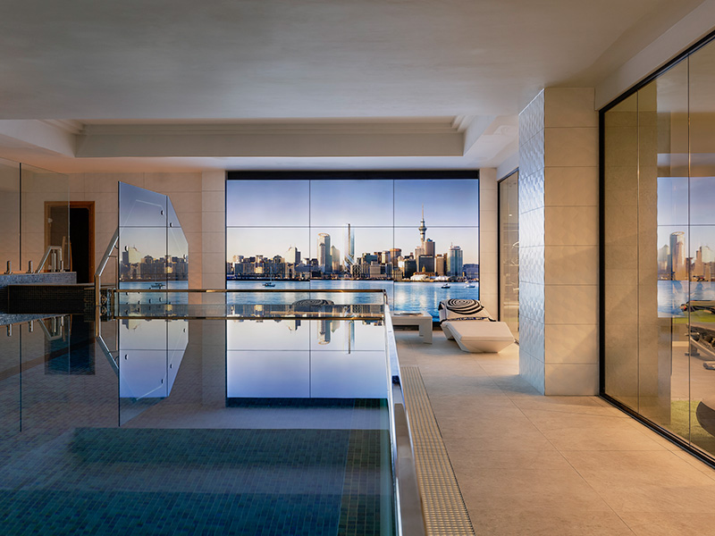 Indoor swimming pool with floor to ceiling windows showing a city skyline at dusk