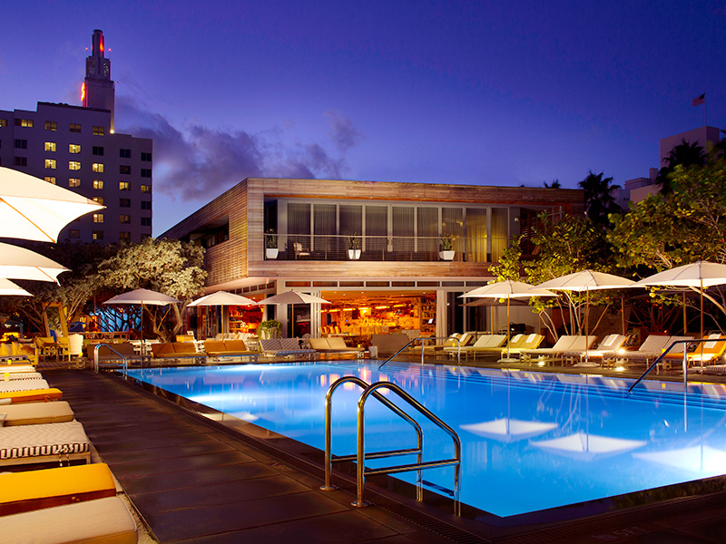 A lit up swimming pool at night, with sun loungers around the edge
