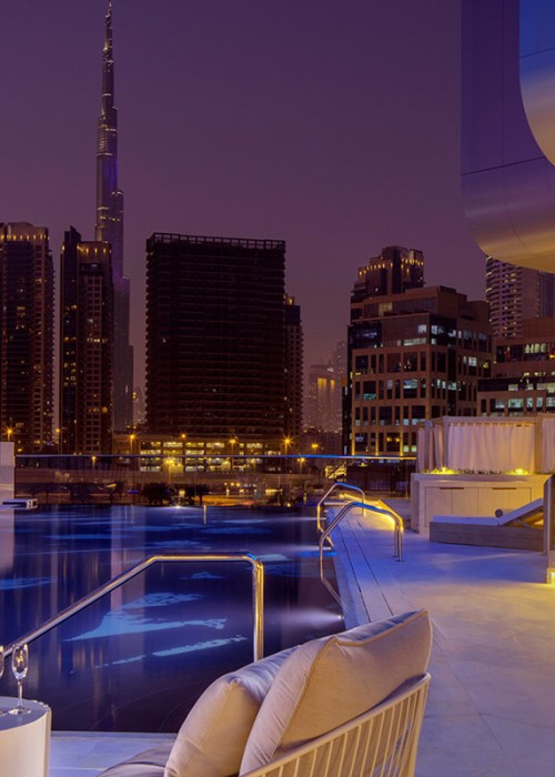 Outdoor terrace with swimming pool with a backdrop of Dubai cityscape at night, including the Burj Khalifa