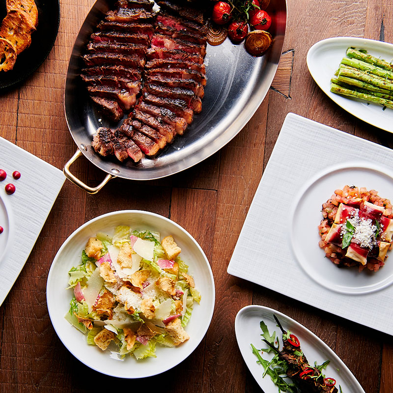 Various plates of food served on a table, including steak and a caeser salad