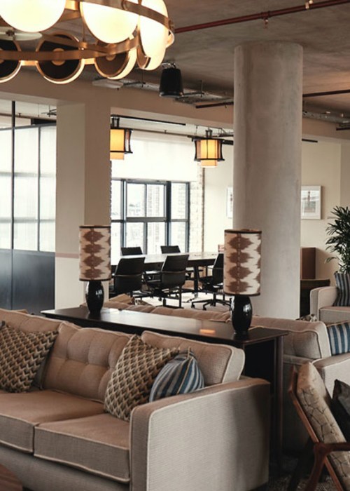 An empty coworking space with sofas and lounge chairs in the middle, and open offices around the edge